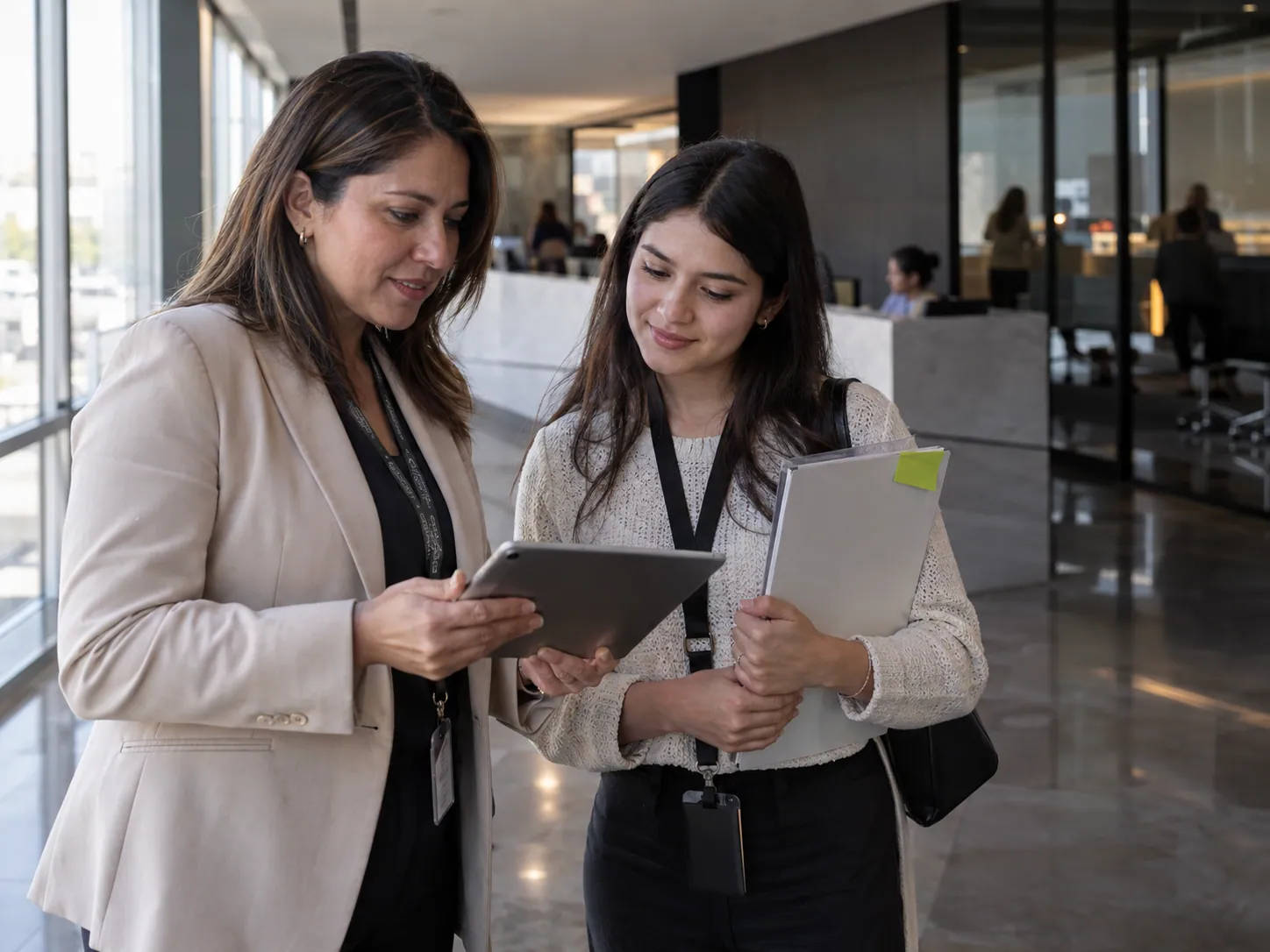 Una responsable de capacitación recibe a una nueva colaboradora y le muestra su ruta de aprendizaje en una tablet.